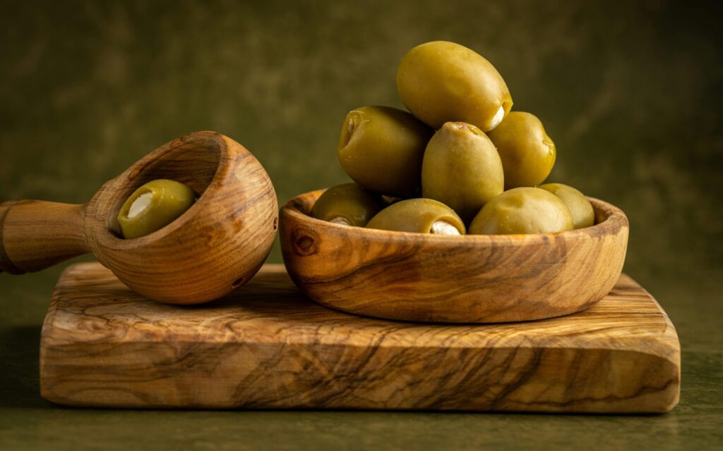 A close-up of green olives in a beautifully crafted wooden bowl and board.