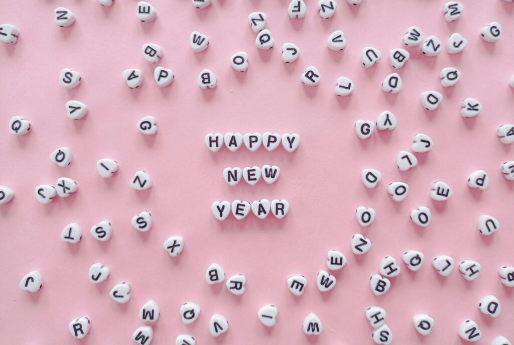 Heart-shaped letter tiles form 'Happy New Year' on a pink background. Minimalist and festive.