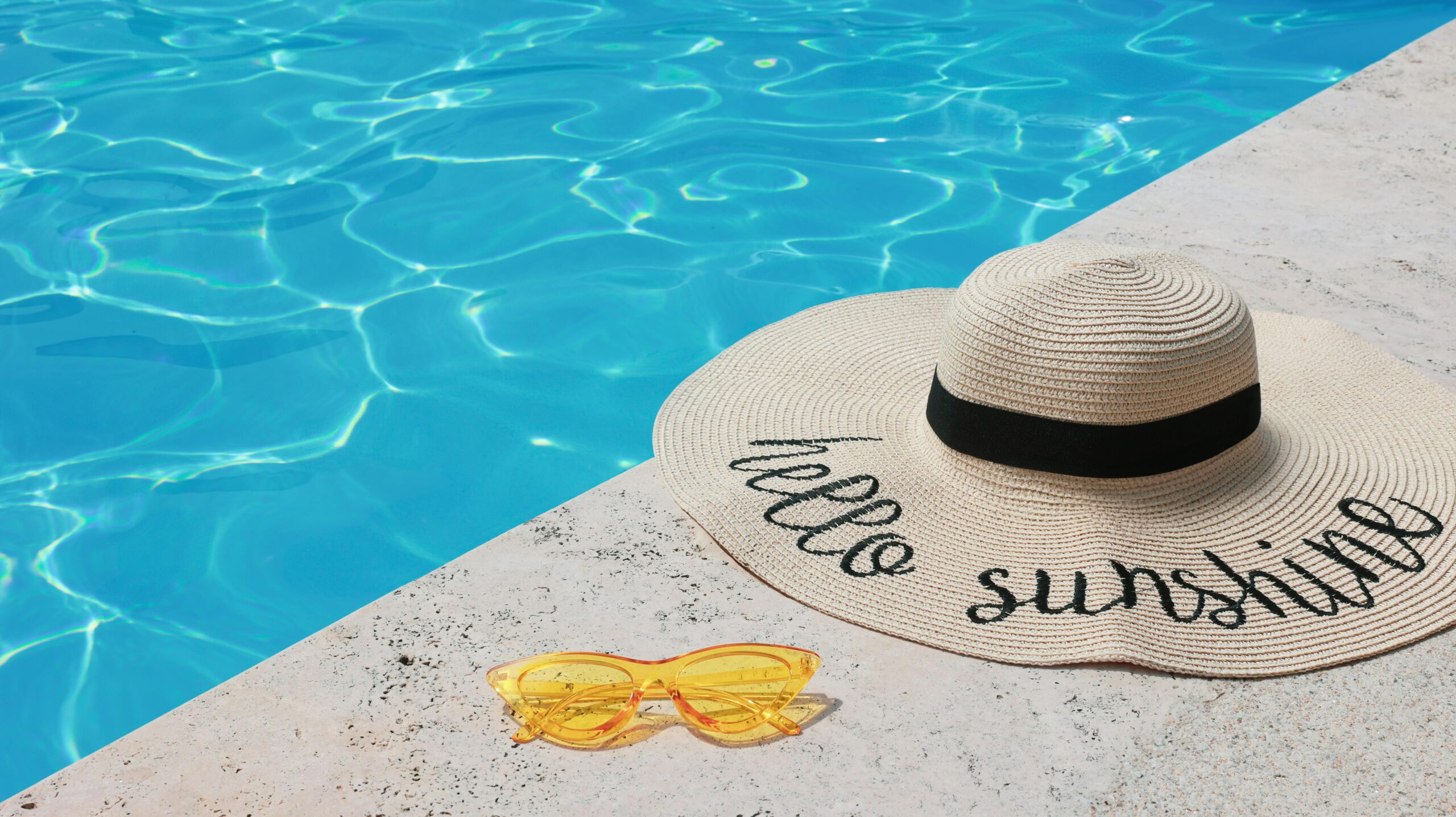 Elegant straw hat and yellow sunglasses beside a shimmering pool, embodying summer relaxation.