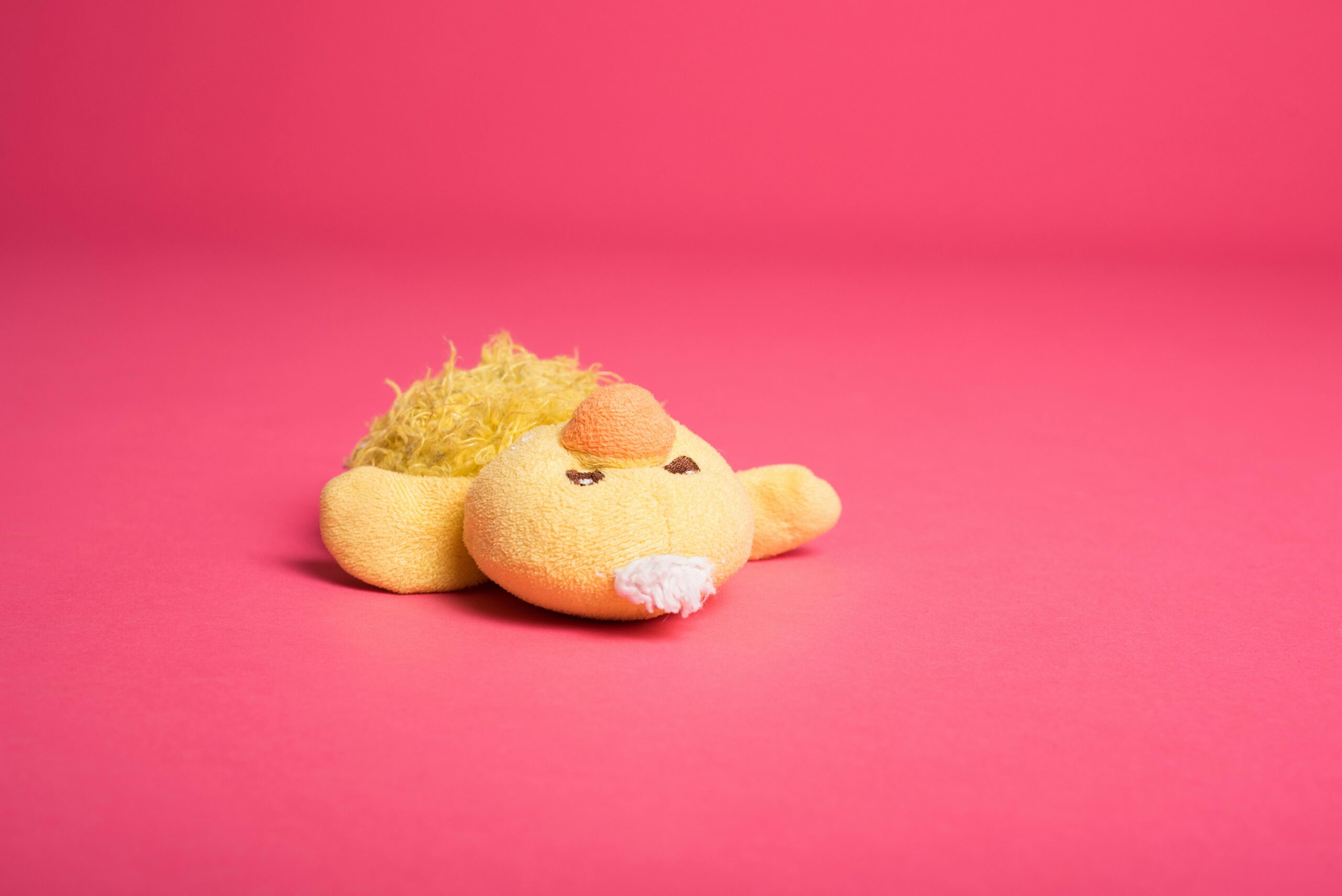 A cute yellow plush toy lying on a bright pink background, ideal for children's themes.