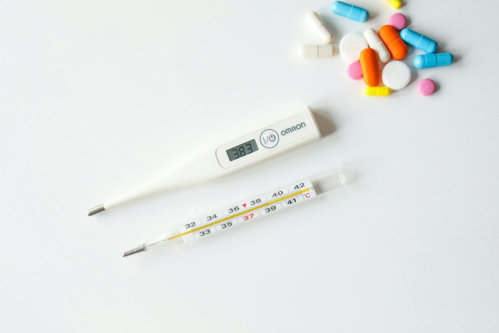 Digital and glass thermometers with colorful pills on white background.