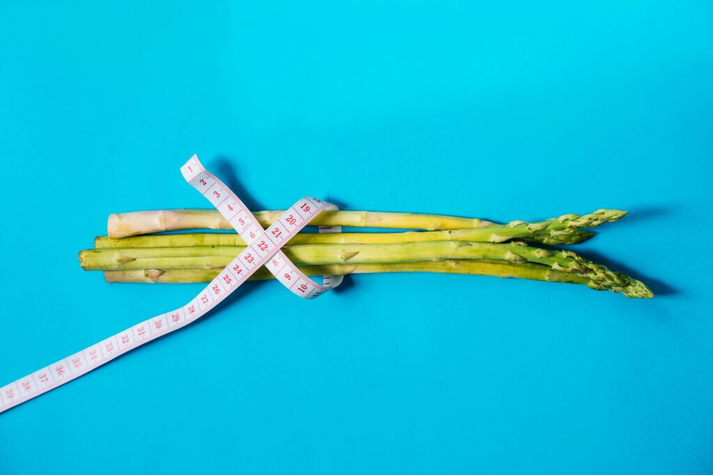 Fresh asparagus wrapped with measuring tape on a vibrant blue background.