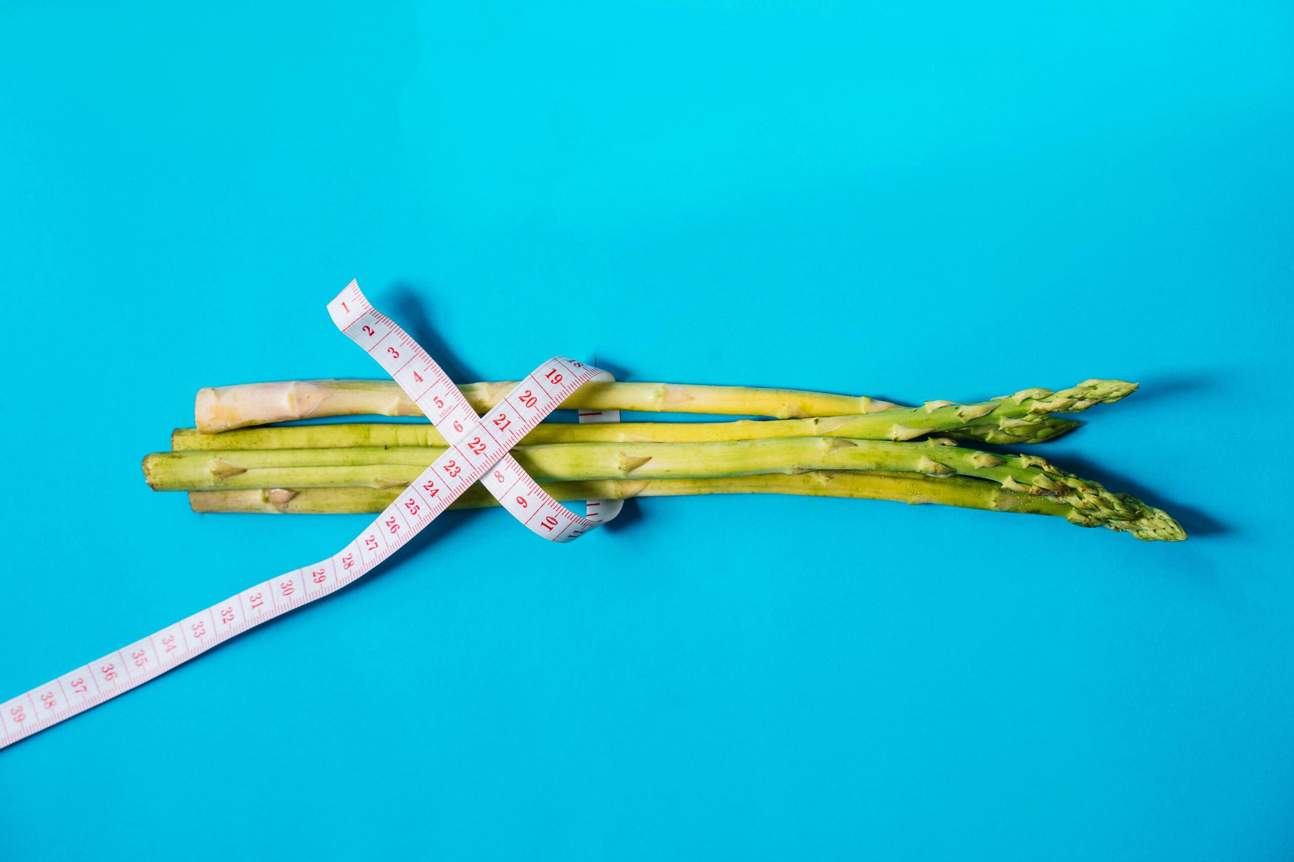 Fresh asparagus wrapped with measuring tape on a vibrant blue background.