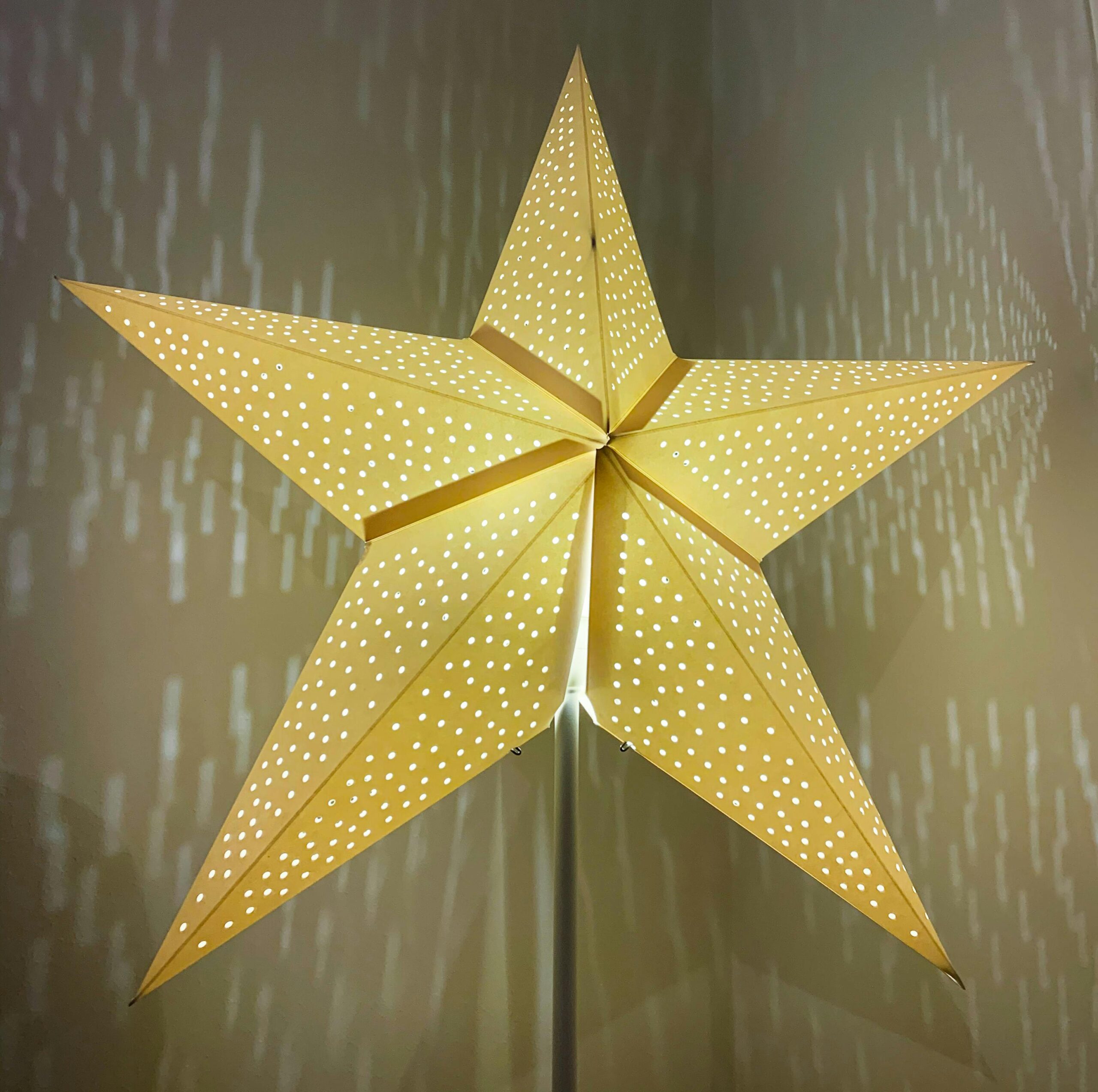 A warm glowing paper star lantern casting decorative patterns on an indoor wall.