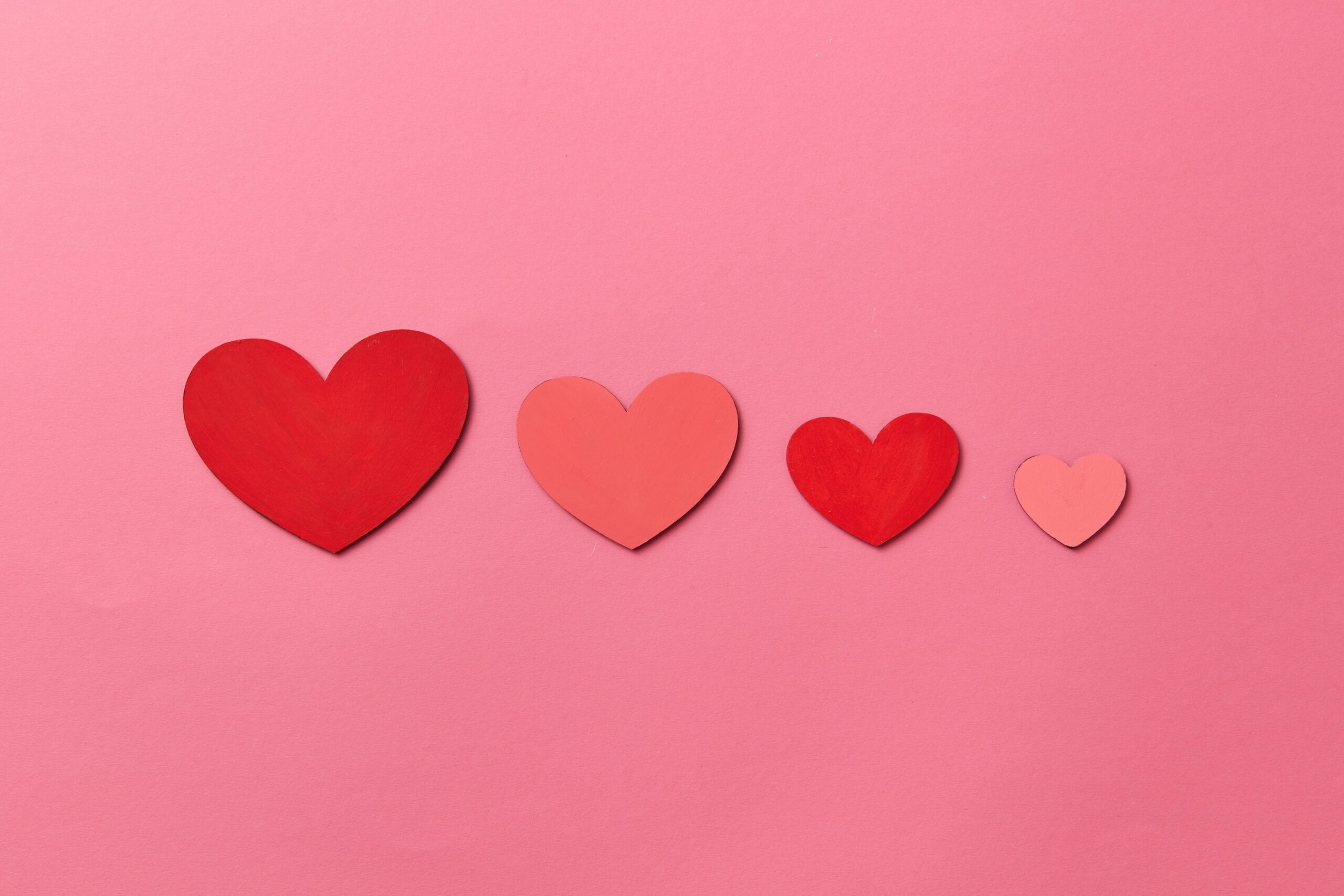 Row of red and pink paper hearts on a pink background symbolizing love and affection.