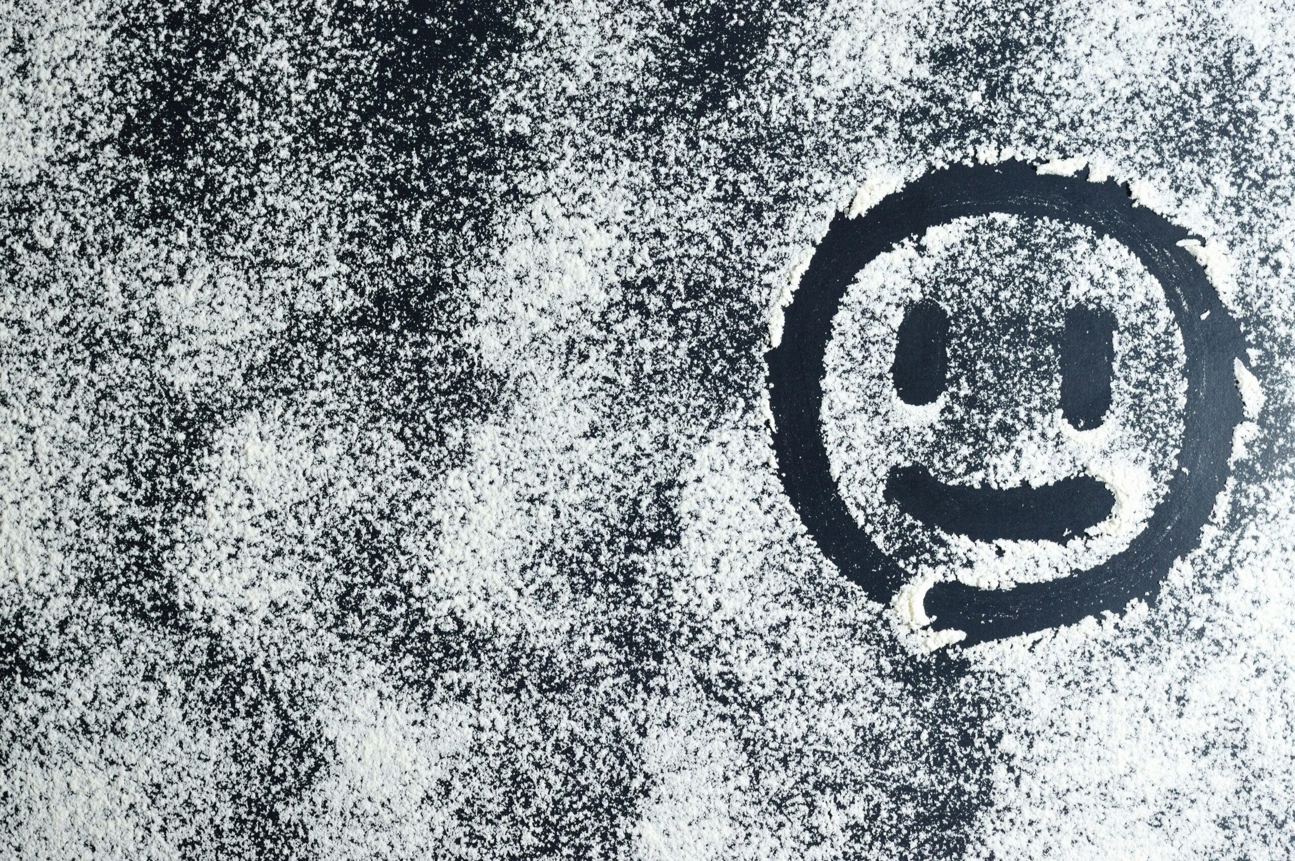 Artistic smiley face drawn through white powder on a black surface, creating an abstract texture.